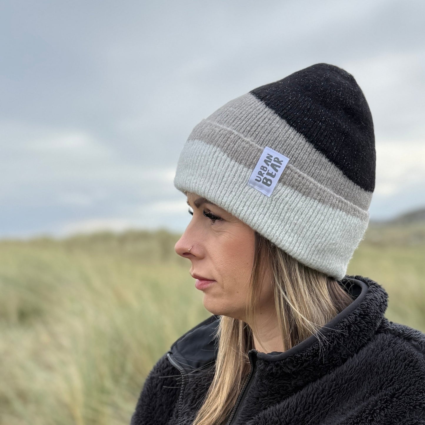 Person wearing a two-tone beanie and black jacket in a natural setting