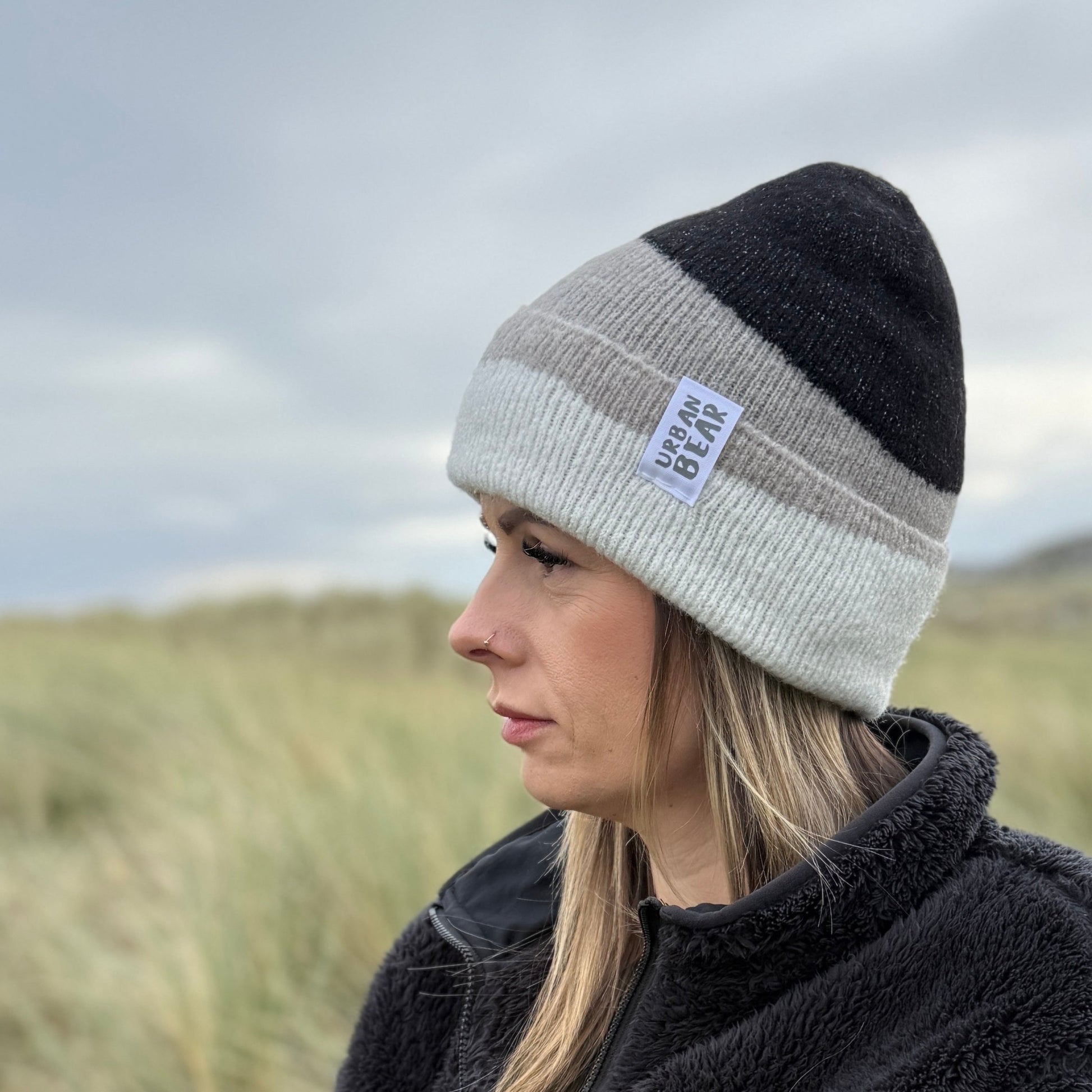 Person wearing a two-tone beanie and black jacket in a natural setting