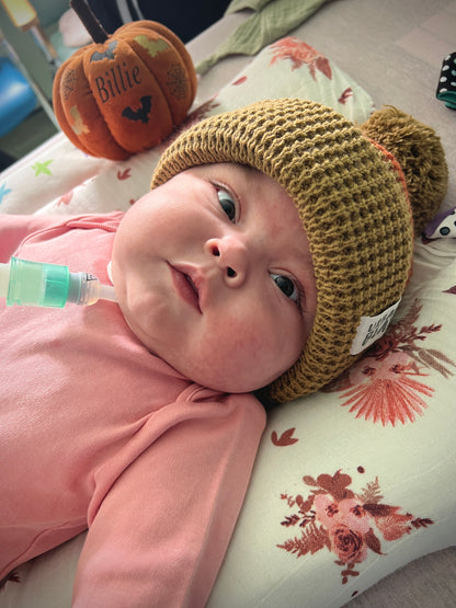 Baby wearing a knitted hat, lying on a floral blanket.
