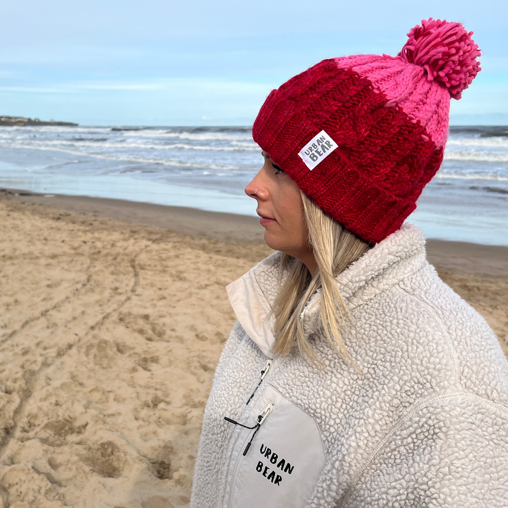 Person wearing a red beanie and light gray jacket on a beach with ocean and sky in the background