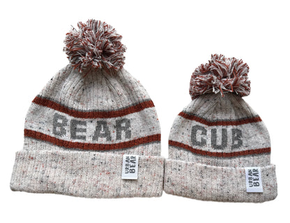 Two grey beanie hats with orange stripes and pom-poms on a white background.