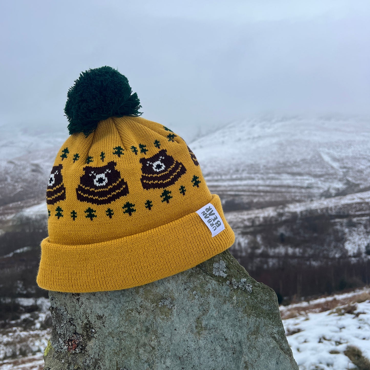 Yellow beanie with bear design and green pom-pom on a stone surface