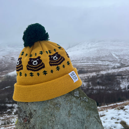 Yellow beanie with bear design and green pom-pom on a stone surface